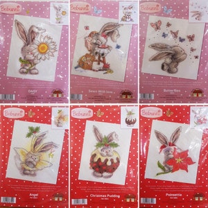 May include: Six cross-stitch patterns featuring a bunny rabbit in various settings. The patterns include a bunny with a daisy, a bunny sewing, a bunny with butterflies, a bunny with angel wings, a bunny with a Christmas pudding, and a bunny with a poinsettia.