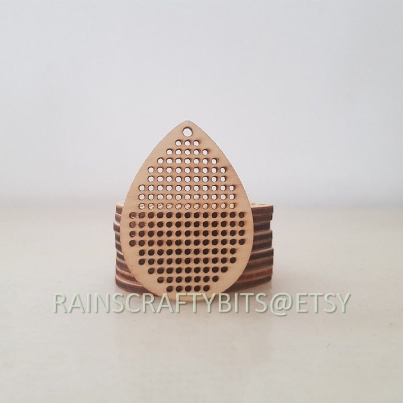 May include: A stack of unfinished wooden teardrop-shaped earring blanks with a perforated design. Each blank has a small hole at the top for hanging. The text "RAINSCRAFTYBITS @ ETSY" is printed at the bottom.