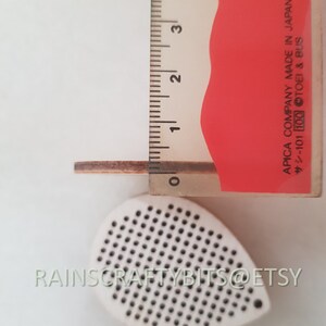 May include: A wooden teardrop-shaped craft supply with a perforated surface, next to a ruler showing a thickness of approximately 0.08 inches. The text "RAINSCRAFTYBITS@ETSY" is visible. A red and white ruler is also present.