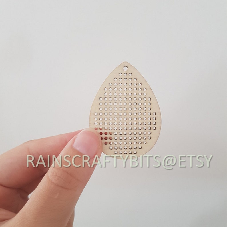 May include: A teardrop-shaped wooden craft pendant with numerous small, evenly spaced holes. The pendant is a light tan color and has a small hole at the top for hanging. The text "RAINSCRAFTYBITS@ETSY" is printed on the bottom of the image.