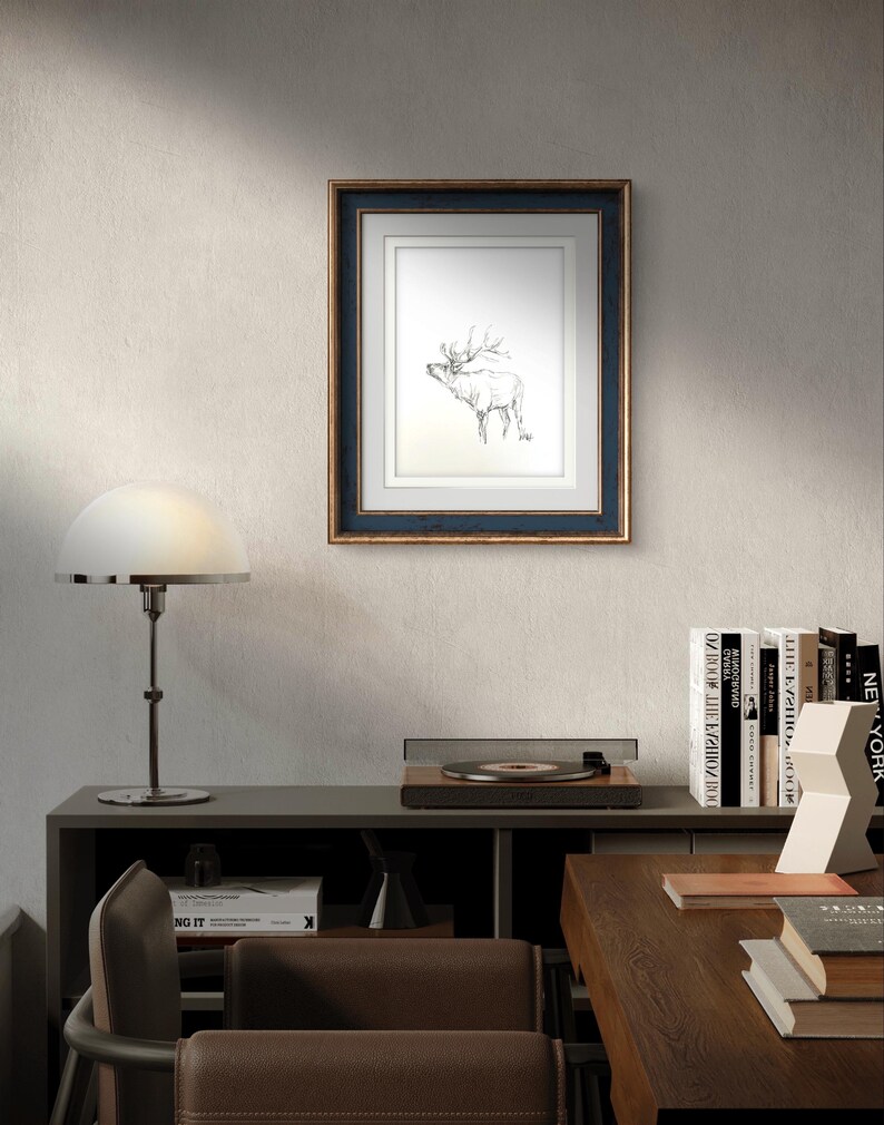 May include: A framed black and white line drawing of a deer with antlers, hanging on a light gray wall. The frame is dark blue with a gold trim.
