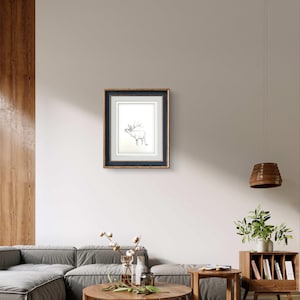 May include: A framed black and white line drawing of a deer with antlers, hanging on a white wall in a living room setting.