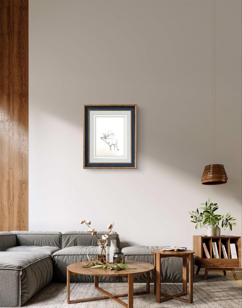 May include: A framed black and white line drawing of a deer with antlers, hanging on a white wall in a living room setting.