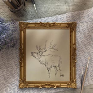 May include: A framed black and white pencil sketch of an elk with large antlers, set against a light beige background. The frame is ornate and gold in color.