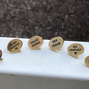 Può includere: Sei spille in smalto color oro con disegni a forma di fumetto. Le spille presentano il seguente testo: "Endless Screaming", "Do Not Perceive Me", "Feelin' Buzzed", "404 Error", "Bee Yourself!" e "Quit Bucc'in Me".