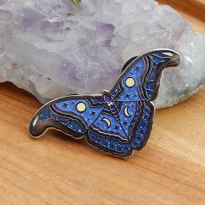 May include: A blue and purple enamel pin of a butterfly with a moon and stars design. The butterfly has a glittery finish.