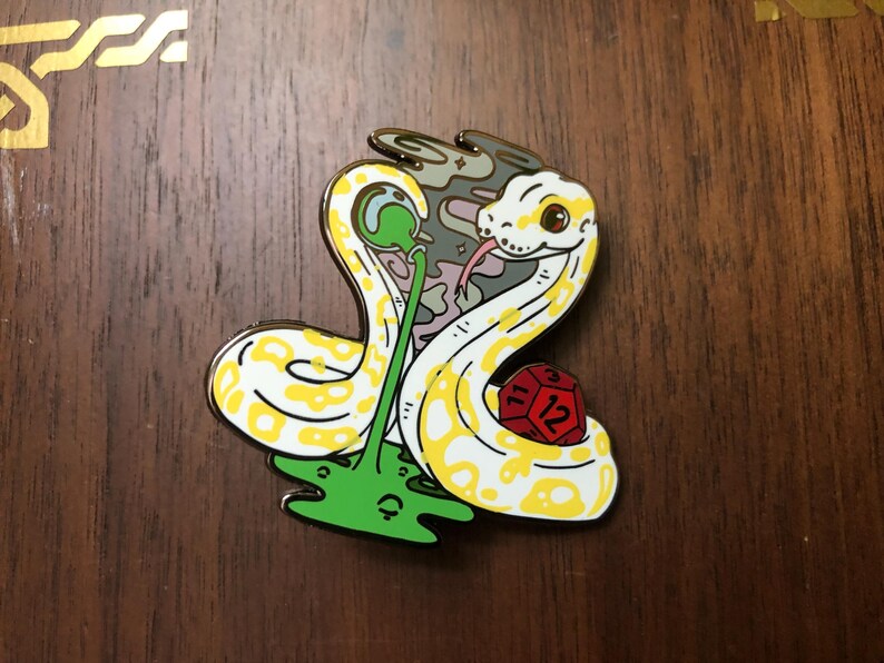 May include: A yellow and white snake with a red and yellow dice in its coils. The snake is curled around a green plant with a purple and grey background. The snake has a black eye and a pink tongue.