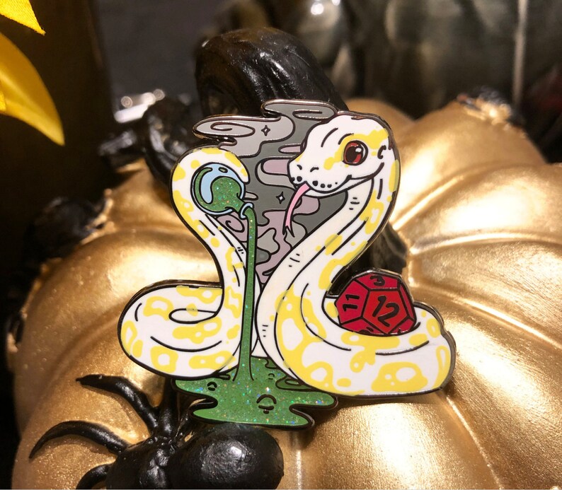 May include: A yellow and white snake with a red and white dice, a green and blue orb, and a pink and grey cloud design. The snake is curled around the dice and the orb is in its mouth. The snake is on a green and white background.