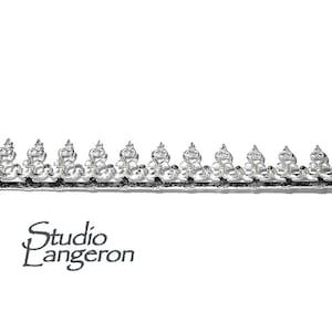 Puede incluir: Borde decorativo plateado con un patrón repetitivo de hojas y espirales estilizadas.