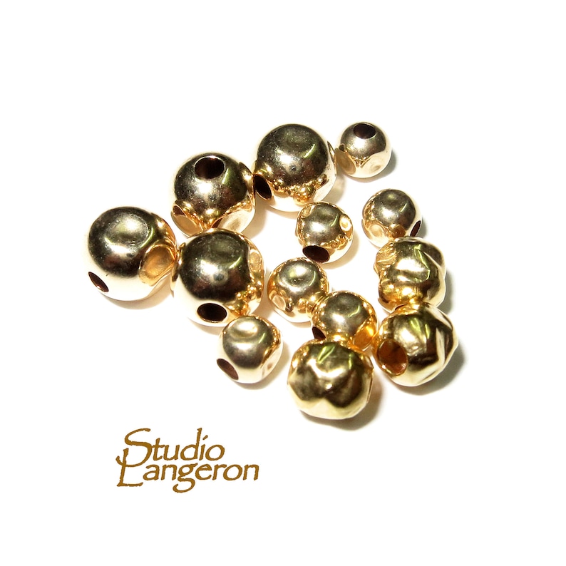 May include: A collection of gold-colored metal beads with holes in the center. The beads are various sizes and shapes, some are round and some are faceted.