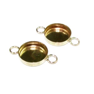 Puede incluir: Dos engastes de bisel de metal dorado con dos bucles a cada lado. Los engastes son redondos y tienen un acabado liso y brillante.