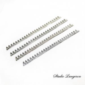Peut inclure: Quatre bandes métalliques argentées avec un motif décoratif répété de petites couronnes stylisées. Les bandes sont disposées en diagonale sur un fond blanc. Le logo Studio Langeron est en bas à droite.