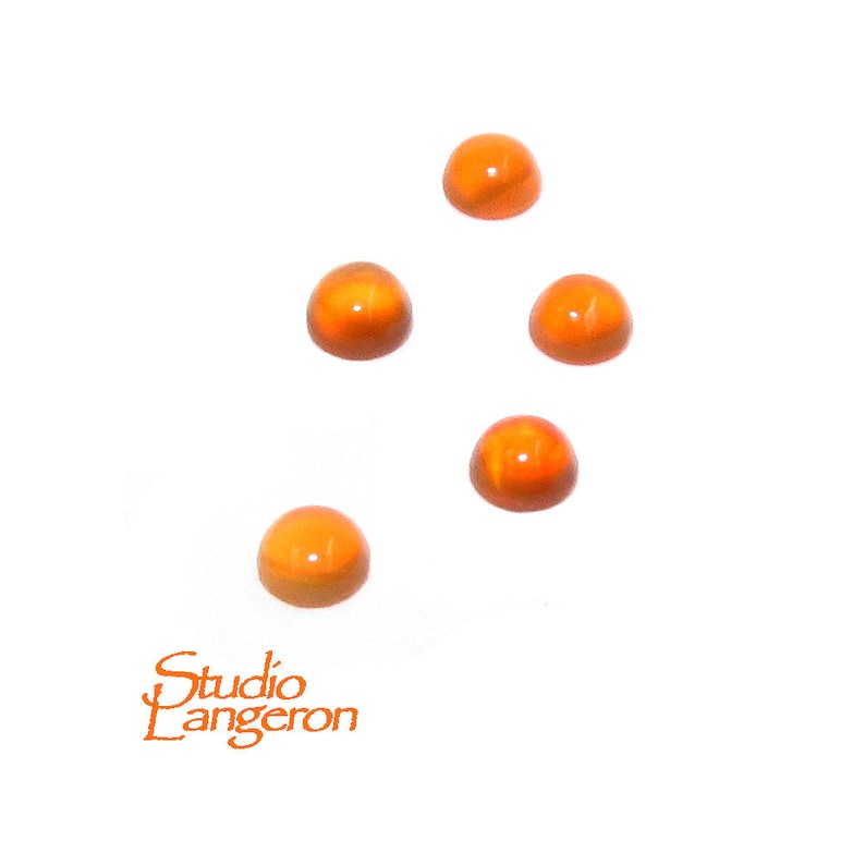 May include: Five orange glass cabochons, each with a slightly different shade of orange, are scattered on a white background.