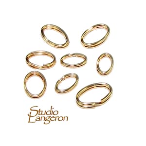 May include: Eight gold-toned oval jump rings of varying sizes. The jump rings are arranged in a scattered pattern on a white background.