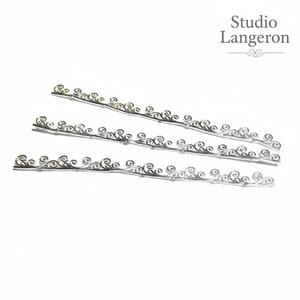 May include: Three silver-colored, decorative metal strips with a repeating swirl design. The strips are arranged diagonally against a white background. The text "Studio Langeron" is in the upper right corner.