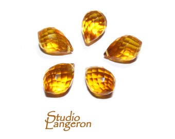 May include: Five faceted teardrop-shaped beads in a golden yellow colour. The beads are arranged in a starburst pattern on a white background.