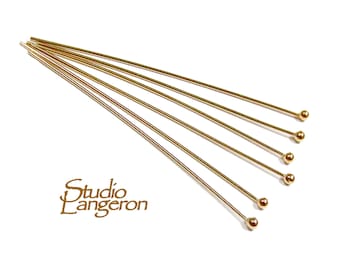 May include: Six gold head pins with round heads. The pins are arranged in a fan shape.