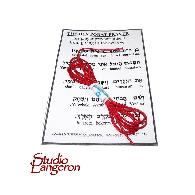 K&ouml;nnte beinhalten: Eine rote Schnur mit einer kleinen israelischen Flagge daran. Die Schnur ist um eine wei&szlig;e Karte mit hebr&auml;ischem Text und den Worten "The Ben Porat Prayer" und "This prayer prevents others from giving us the evil eye." gewickelt.
