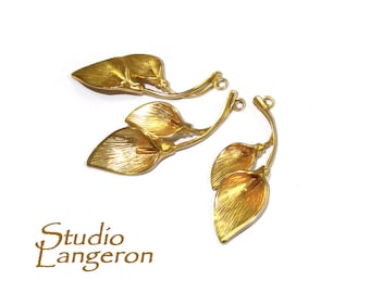 May include: Three gold-toned metal leaf charms with a loop at the top for attaching to jewelry or other crafts. The leaves are arranged in a cluster of two and one, with a stem connecting them.