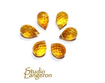 May include: Seven faceted teardrop shaped gemstones in a yellow colour. The gemstones are arranged in a circle on a white background.