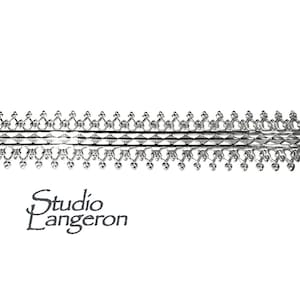 Könnte beinhalten: Silberne Metallverkleidung mit einem filigranen, komplizierten Design. Die Verkleidung weist ein sich wiederholendes Muster aus kleinen, abgerundeten Formen und einer zentralen Reihe größerer, aufwendigerer Formen auf.