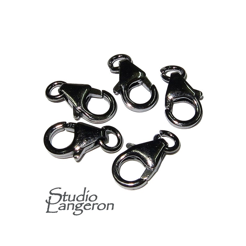May include: Five silver-colored lobster claw clasps. Each clasp has a spring-loaded lever and a small ring for attaching to jewelry or other items. The clasps are arranged on a white background. The Studio Langeron logo is in the bottom left corner.