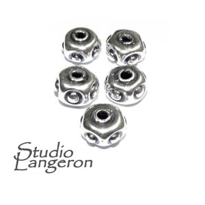 May include: Five silver metal beads with a decorative design. Each bead has a round hole in the center and a raised pattern of circles around the hole.
