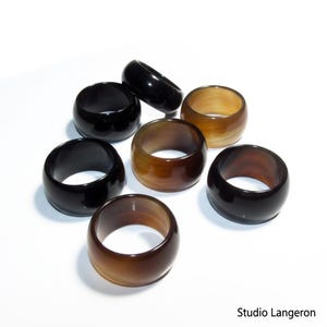 Puede incluir: Una colección de siete servilleteros redondos y gruesos en varios tonos de marrón y negro. Los anillos están hechos de un material pulido, con un acabado brillante. Los servilleteros están dispuestos sobre una superficie blanca.