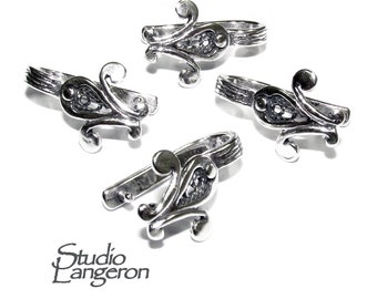 Pode incluir: Quatro anéis de metal prateado com um design ornamentado e rodopiante. Cada anel apresenta um elemento decorativo com um padrão central de filigrana e detalhes curvos. Os anéis estão dispostos sobre um fundo branco. O texto "Studio Langeron" é visível.