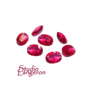 Può includere: Sette pietre preziose ovali di colore rosso vivo. Le pietre preziose sono sfaccettate e hanno una finitura lucida.