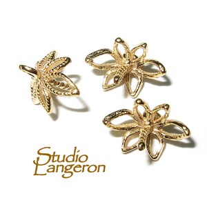 May include: Three gold-colored metal flower-shaped bead caps. The caps have a delicate, intricate design.