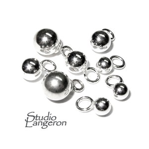 Op de afbeelding: Een set zilveren balbedels met springringen. De bedels zijn in verschillende maten, waarbij de grootste ongeveer 2,5 cm in diameter is.