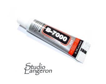 Op de afbeelding: Een tube B-7000 multifunctionele lijm. De tube is zilverkleurig met zwarte en rode tekst, waaronder "B-7000" en "0,1 fl.oz (3ml)". De witte dop zit linksboven. Het Studio Langeron-logo staat onderaan.