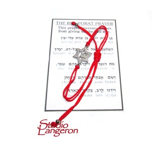 Può includere: Un braccialetto con cordino rosso con un ciondolo a forma di Stella di David, esposto con una carta con testo ebraico e traduzione inglese. Il ciondolo è color argento e decorato con piccole pietre trasparenti. La carta recita "THE BIPORAT PRAYER".