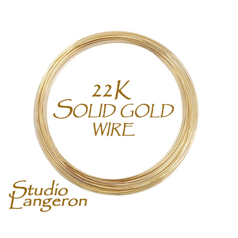 May include: A spool of 22K solid gold wire, tightly wound in a circular shape. The wire is a bright, shiny gold color. The text "22K SOLID GOLD WIRE" is printed in a brown font. The Studio Lanceron logo is also visible.