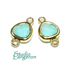 May include: Two gold-tone metal connector charms with a light blue glass stone in the center. The charms have two loops on each side.
