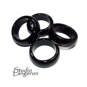 Pode incluir: Quatro anéis de ônix preto, cada um com um acabamento liso e polido. Os anéis estão empilhados uns sobre os outros, criando uma exibição visualmente atraente.
