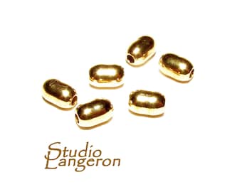 May include: Six gold-colored metal beads, each with a hole in the center, are scattered on a white surface. The beads are oval-shaped and have a smooth, shiny finish.