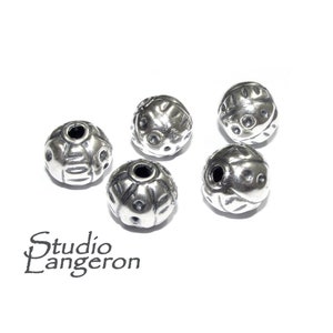 May include: Five silver round beads with a textured surface and a hole in the center.