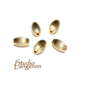 May include: Five gold-colored metal beads with a ribbed texture. The beads are oval shaped.