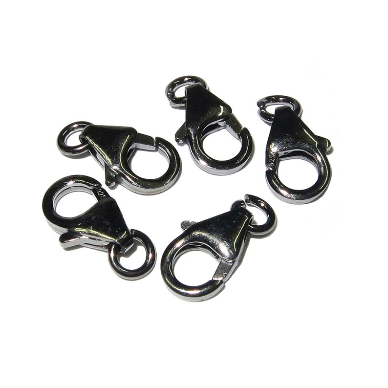 May include: Five gunmetal-colored lobster clasps are arranged on a white background. Each clasp has a spring-loaded mechanism and a small ring for attaching to jewelry or other items. The clasps are made of a shiny, metallic material.