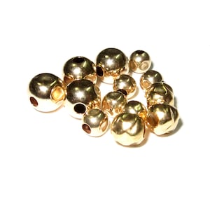 May include: A group of gold-colored metal beads with a hole in the center of each bead. The beads are arranged in a loose pile.