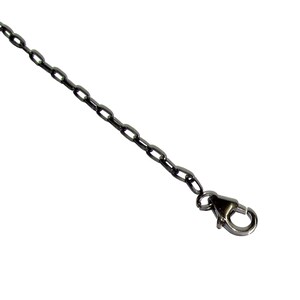 May include: A dark gray metal chain with oval links and a lobster clasp. The chain is angled across a white background, showcasing its sleek design and metallic finish. Ideal for jewelry making or as a decorative element.
