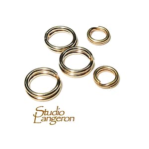 May include: Five gold-coloured double split rings of varying sizes are arranged on a white background. The rings are open, showing the split. The Studio Langeron logo is in the bottom left corner.