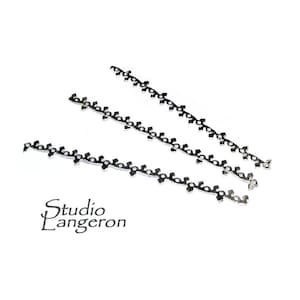 Puede incluir: Tres cadenas de ortodoncia plateadas con un patrón decorativo. Las cadenas están dispuestas en fila sobre un fondo blanco.