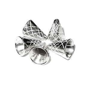Op de afbeelding: Vijf zilveren metalen kegelvormige kralencaps met een kruislings patroon. De caps zijn in een cirkel op een witte achtergrond gerangschikt.