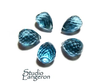 May include: Five teardrop-shaped blue topaz gemstones, each with a faceted cut, arranged in a starburst pattern on a white background.