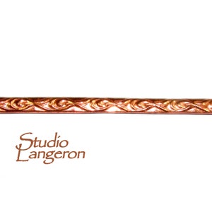 May include: A close-up of a copper wire with a decorative wave pattern. The wire is on a white background.