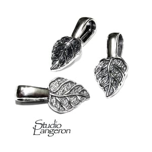 May include: Three silver leaf-shaped pendant clasps with a textured surface. The clasps have a loop at the top for attaching to a necklace or bracelet.