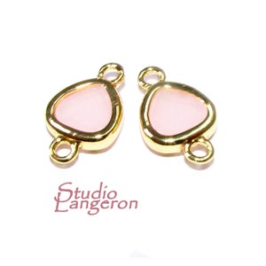 May include: Two gold-tone metal connector charms with a pink glass centre in the shape of a teardrop. The charms have two jump rings on each side.